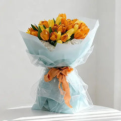 Vibrant orange and yellow tulip bouquet wrapped in light blue paper with orange ribbon, perfect for flower delivery