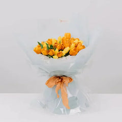 Vibrant yellow tulip bouquet wrapped in light blue paper with orange ribbon, perfect for flower delivery