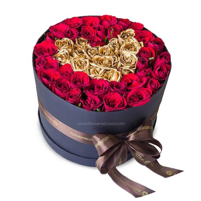 Luxury flower delivery of red and gold roses arranged in a round box with ribbon