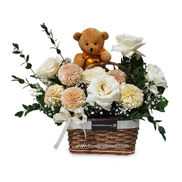 Flower delivery basket with white roses, soft pink blooms, greenery, and a plush teddy bear.