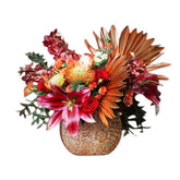 Exotic flower arrangement with red lilies, roses, and orange foliage in vase for delivery