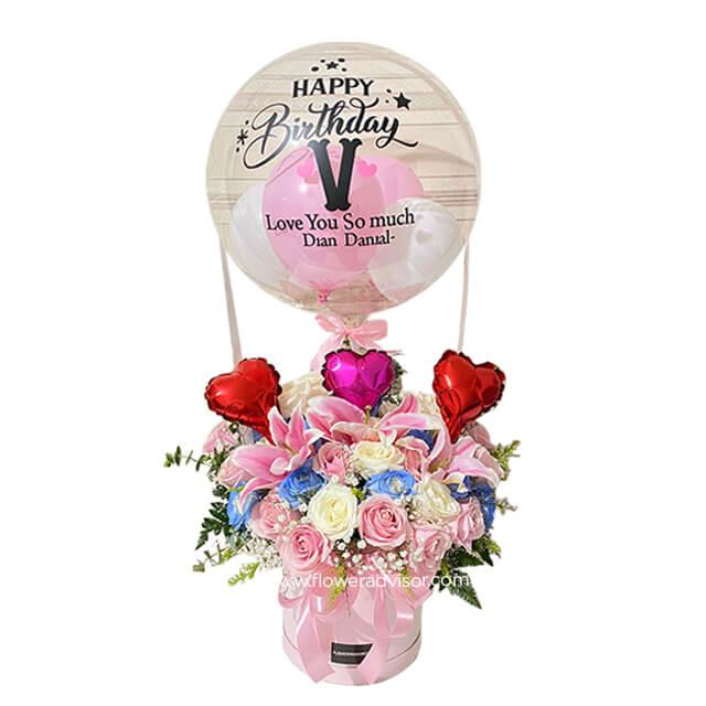 Birthday flower delivery with pink lilies, roses, blue accents, and heart-shaped balloons