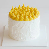 Elegant cake with white frosting and yellow peaks, ideal for cake and flower delivery gifts