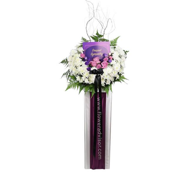Sympathy flower stand with white chrysanthemums, purple roses, and greenery for delivery
