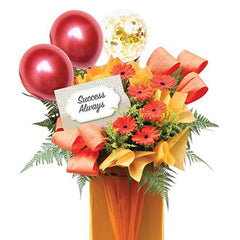 Flower delivery arrangement with red gerbera daisies, festive balloons, and a 'Success Always' card