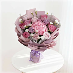 Elegant pink and purple flower bouquet for delivery, arranged in mauve wrapping on a table