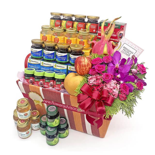Premium flower delivery hamper with fresh pink flowers, fruits, and bottled delicacies