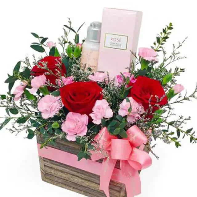 Flower delivery box with red roses, pink carnations, greenery, and a gift set.