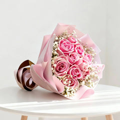 Pink rose bouquet with baby's breath for flower delivery, arranged on a white table.