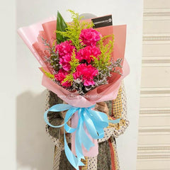Fresh pink flower bouquet with greenery, wrapped in pink paper and blue ribbon for delivery