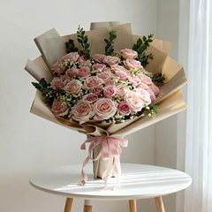 Large bouquet of pink roses in kraft wrapping for flower delivery, displayed on a table