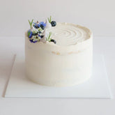 Elegant white cake decorated with fresh flowers and blueberries, perfect for flower delivery in Singapore