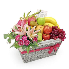 Flower delivery basket with fresh fruit, lilies, carnations, and pink ribbon accent