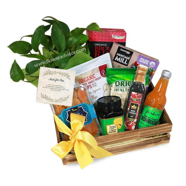 Healthy gourmet gift basket with green plant, snacks, honey, and drinks for flower delivery