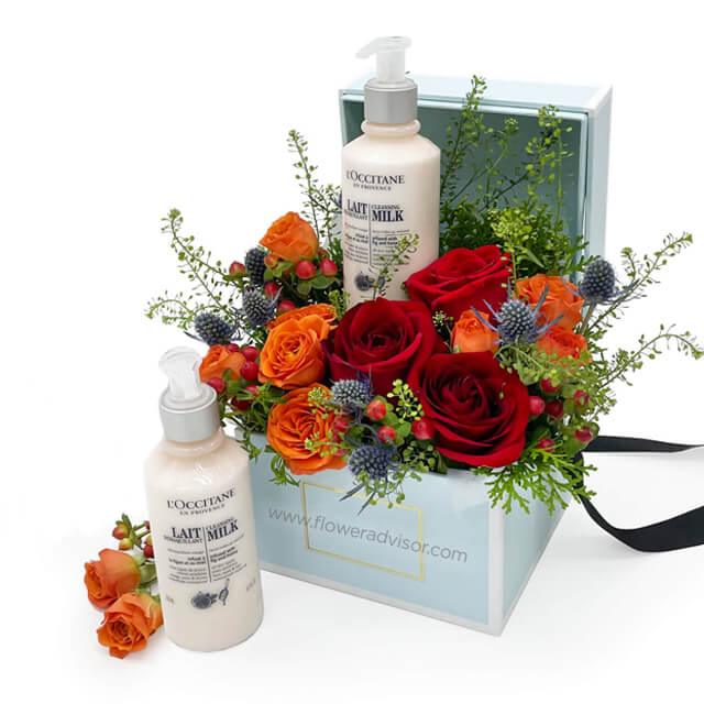Flower delivery gift box with fresh red and orange roses, greenery, and skincare products