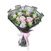 Flower delivery bouquet with pink roses, baby's breath, and greenery wrapped in black with ribbon
