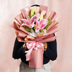 Hand delivering a pink lily bouquet wrapped in pink paper for flower delivery