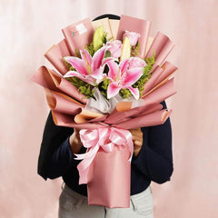 Hand delivering a pink lily bouquet wrapped in pink paper for flower delivery