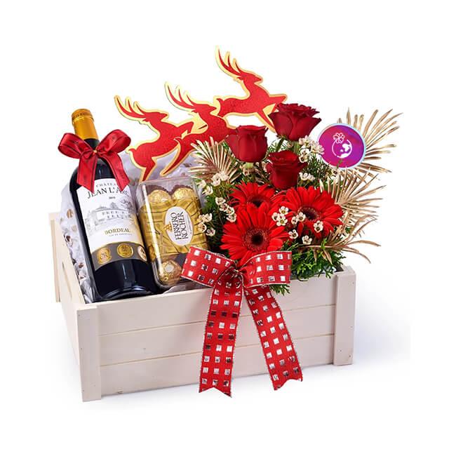 Festive flower delivery hamper with red roses, wine, chocolates, and red ribbon.