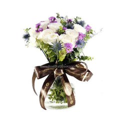 Elegant flower bouquet with white roses, purple asters, and thistles in a glass vase for delivery