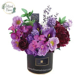Vibrant artificial flower arrangement with purple and red blooms in a black delivery box
