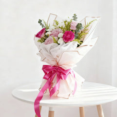 Pastel rose bouquet with pink ribbon, arranged for flower delivery, on a white table