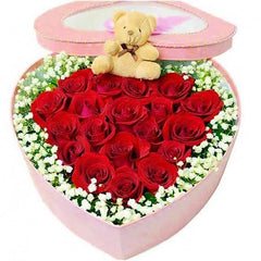 Heart-shaped box with red roses, white flowers, and a small teddy bear for flower delivery