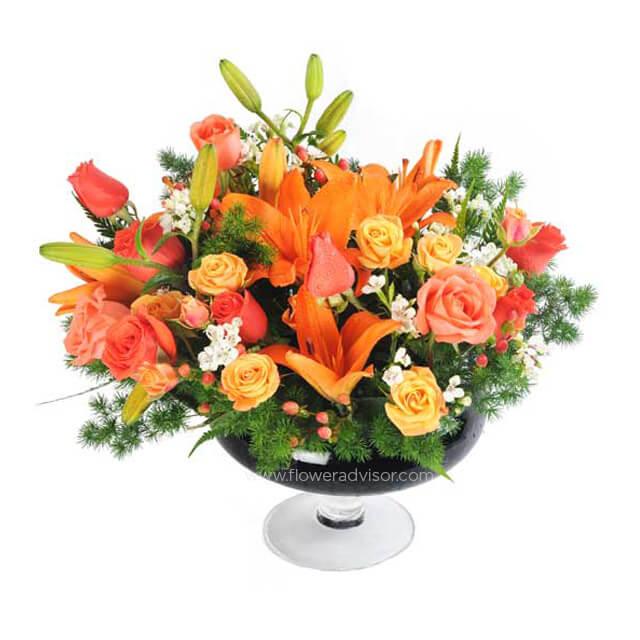 Fresh flower delivery of orange lilies, roses, berries and assorted blooms in a glass vase