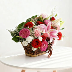 Flower delivery basket with pink lilies, red roses, and mixed fresh blooms on a table
