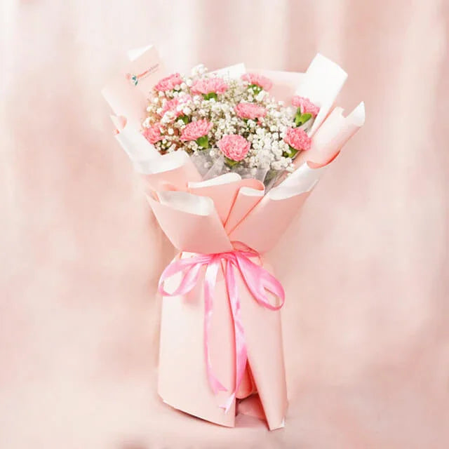 Fresh pink carnation bouquet with baby's breath in pastel paper, ideal for flower delivery.