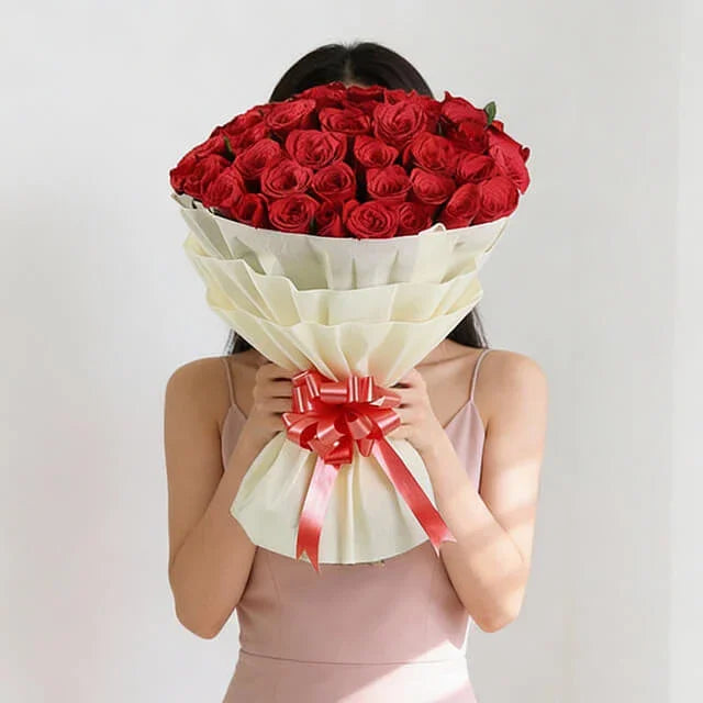 Large bouquet of fresh red roses wrapped with white paper and ribbon, perfect for flower delivery