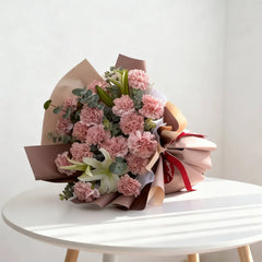 Elegant pink carnation bouquet with lilies for flower delivery on a white table