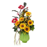 Bright artificial flower arrangement with sunflowers and pink blooms in a green vase for delivery