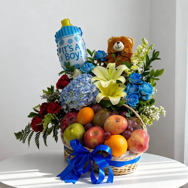 Flower delivery basket with mixed fresh flowers, fruits, teddy bear, and blue ribbon for baby boy