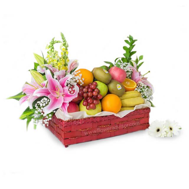 Fruit and flower delivery basket with lilies, roses, grapes, oranges, bananas, and kiwis