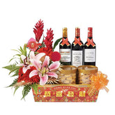 Festive flower arrangement with lilies, red blooms, wine bottles, and treats for delivery