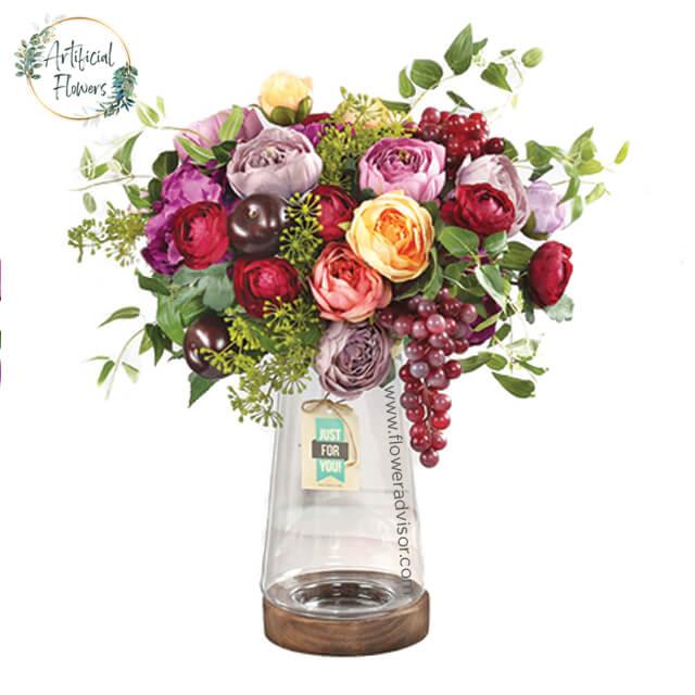 Colorful artificial flower arrangement with greenery and a 'Just for You' tag in a clear vase for delivery