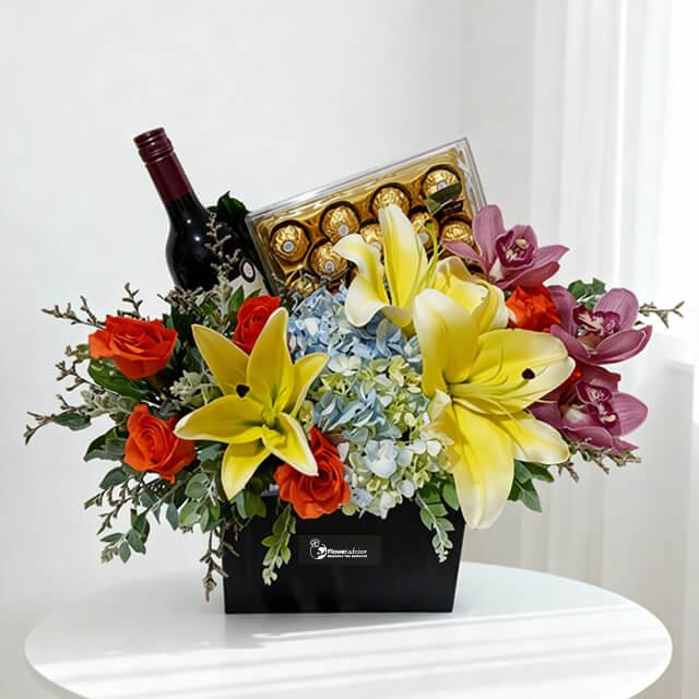 Elegant flower delivery arrangement with lilies, roses, orchids, wine, and chocolates