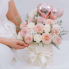 Elegant flower delivery arrangement with pink roses, carnations, and heart balloons in a hatbox.