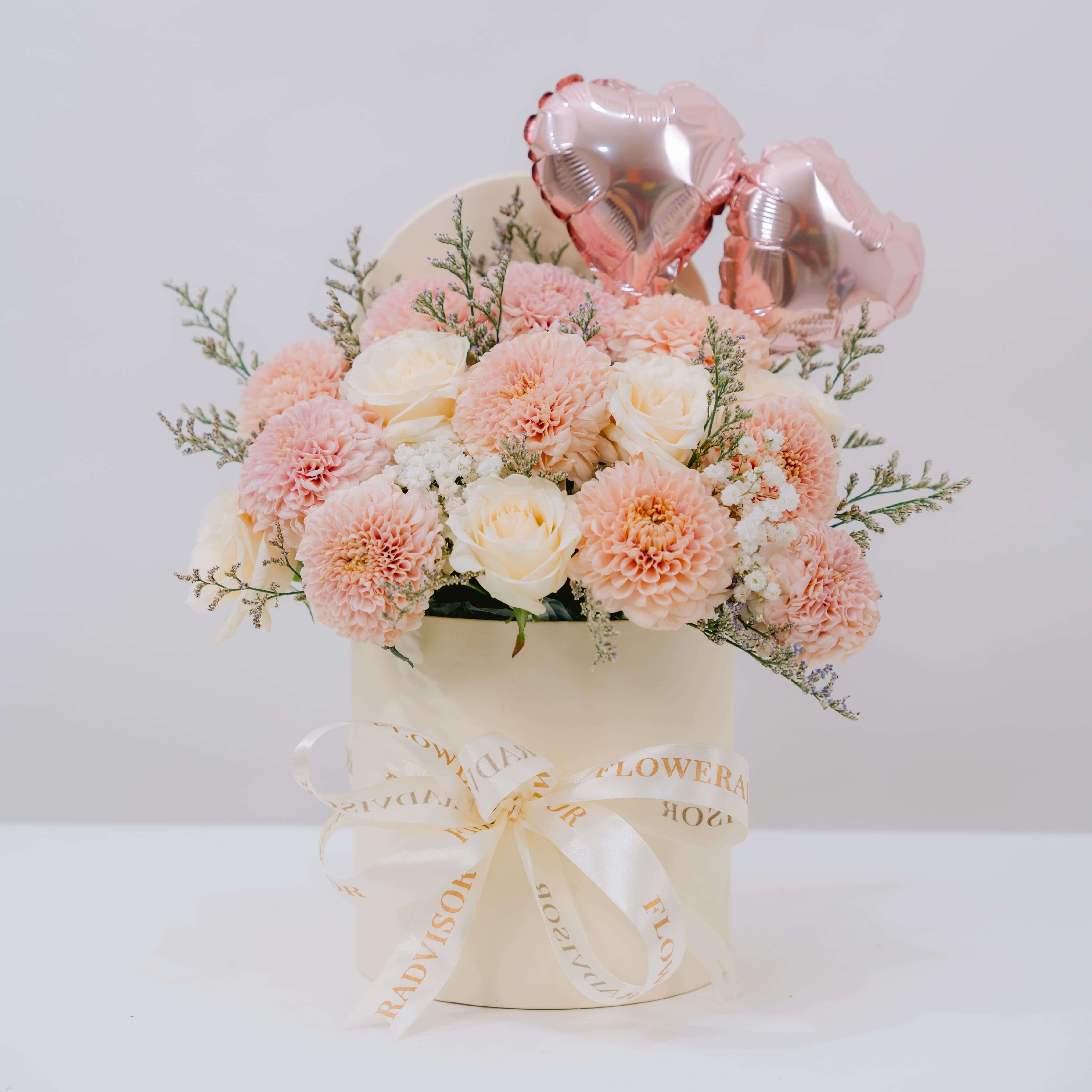 Fresh pastel flower bouquet with roses in a hat box for flower delivery, pink heart balloons