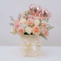 Fresh pastel flower bouquet with roses in a hat box for flower delivery, pink heart balloons
