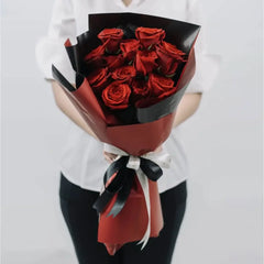 Hand holding bouquet of red roses wrapped in black and red paper for flower delivery