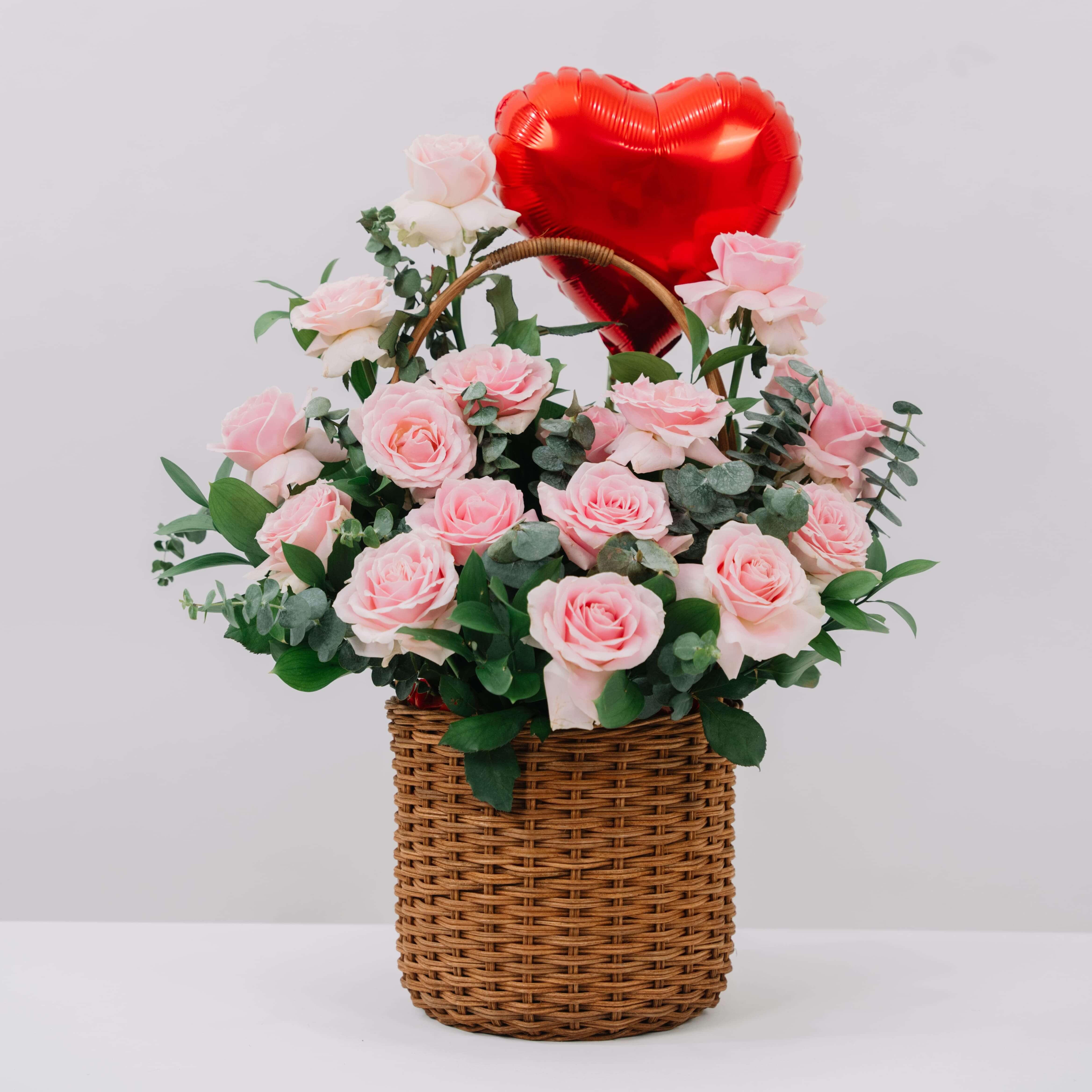 Pink rose bouquet in basket with greenery and heart balloon for flower delivery