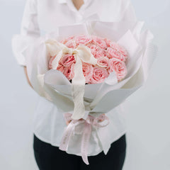 Hand holding a bouquet of pink roses with white ribbon, perfect for flower delivery