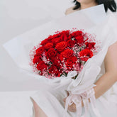 Red rose bouquet with pink baby’s breath for flower delivery, wrapped in white paper.