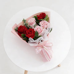 Hand-tied bouquet of red and pink roses with greenery, ideal for flower delivery in Singapore