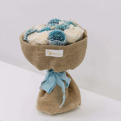 Rustic bouquet with white roses and blue flowers in burlap wrap, perfect for flower delivery