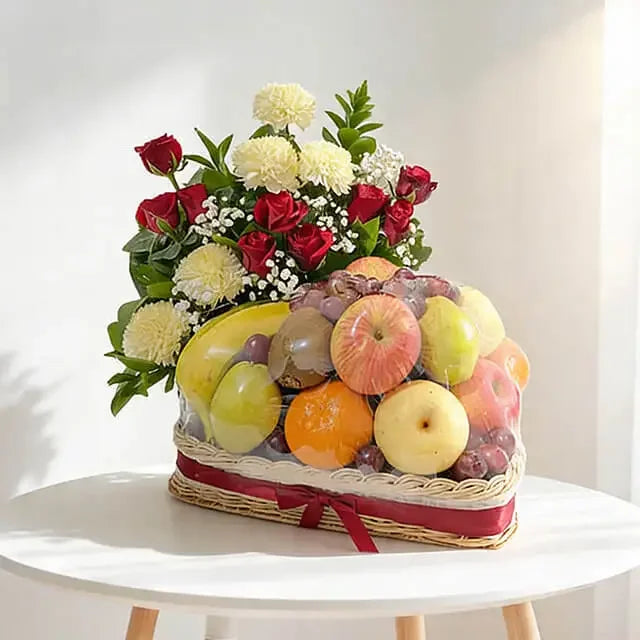Flower delivery basket with red roses, white flowers, and assorted fresh fruits on a table