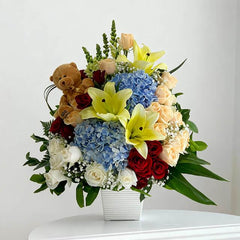Vase arrangement with yellow lilies, blue hydrangeas, red and white roses, teddy bear for flower delivery