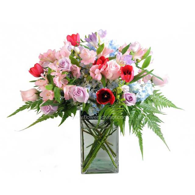 Bouquet of blue hydrangeas, red tulips, pink and purple roses in glass vase for flower delivery
